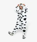 Adult wearing a black and white cow onesie playfully lifting one leg, front view.
